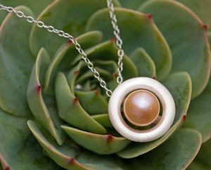Very pretty peach freshwater pearl set in a halo pendant of satin finished sterling silver. Designed and handmade by William White in Cornwall, UK