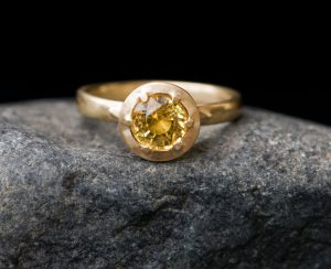 Gold ring with claw set yellow sapphire on grey rock